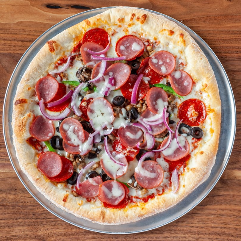 A Verona Italian Cafe pizza with pepperoni, sausage, olives, onions, and green peppers on a metal tray.
