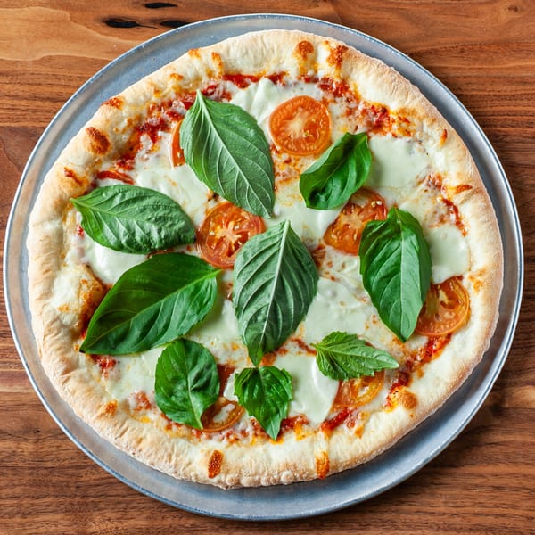 A freshly baked Margherita pizza with melted mozzarella, tomato slices, and fresh basil leaves.