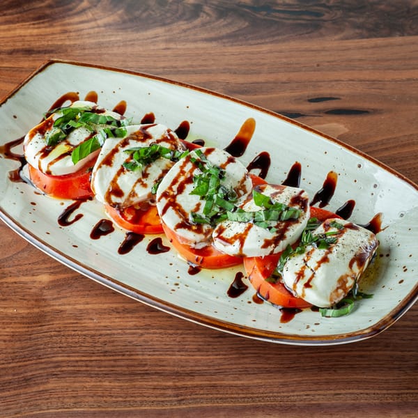 Caprese salad with sliced tomatoes, fresh mozzarella, basil, and balsamic glaze on a white plate.