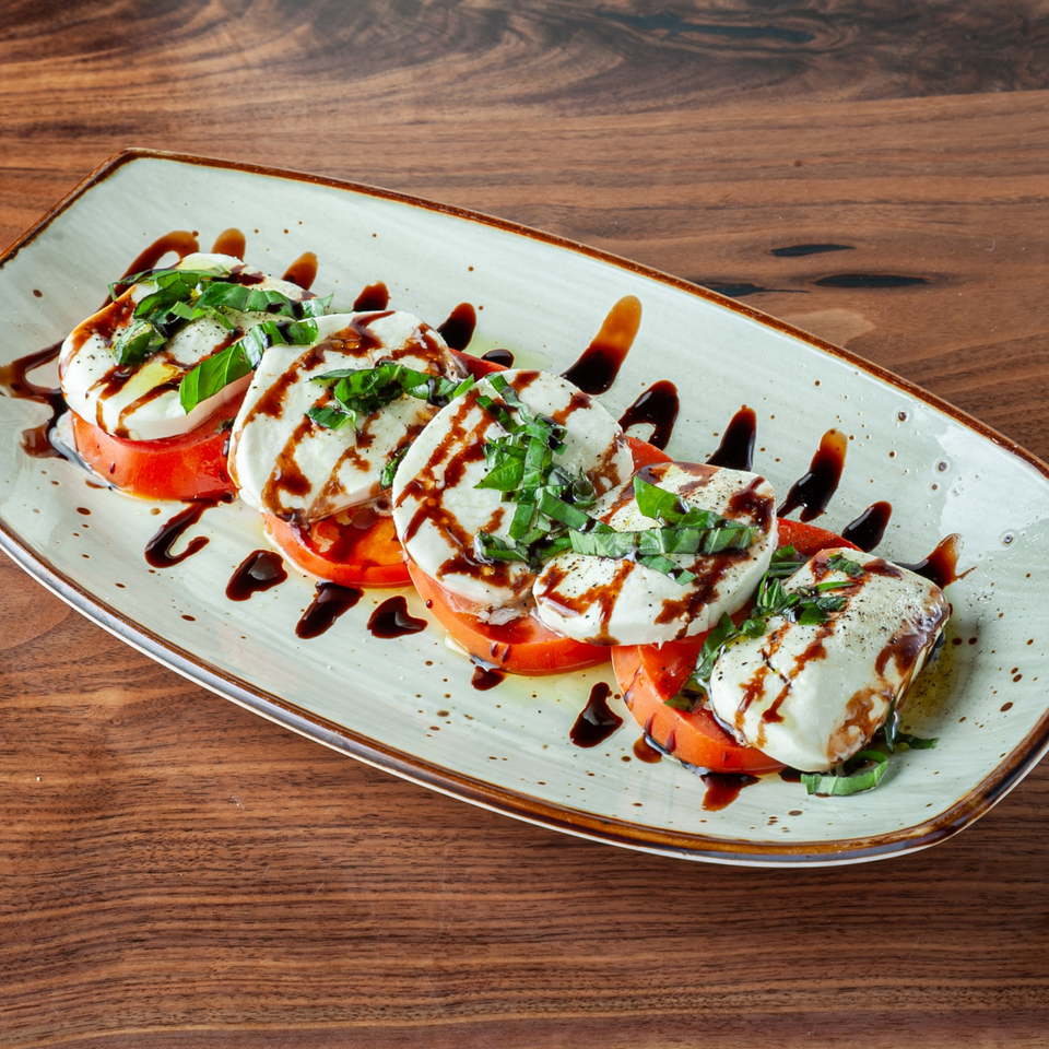 Caprese salad with sliced tomatoes, fresh mozzarella, basil, and balsamic glaze on a white plate.